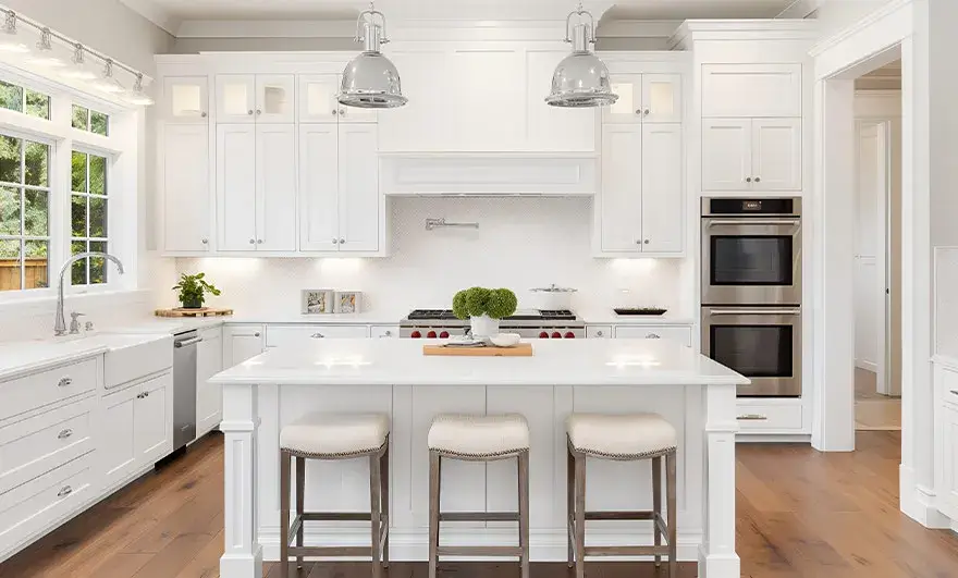 L-shaped modular kitchen design featuring a modern white kitchen with stainless steel appliances and a spacious island, complete with three bar stools for casual dining and socializing.
