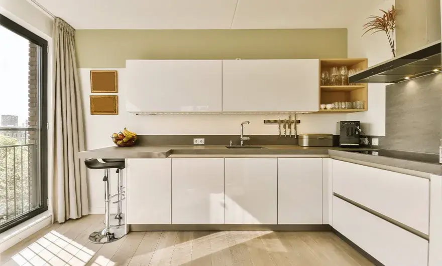 L-shaped modular kitchen design featuring beautiful wood flooring and sleek white cabinetry, illuminated by natural daytime light streaming through the window panes, creating a bright and inviting atmosphere.